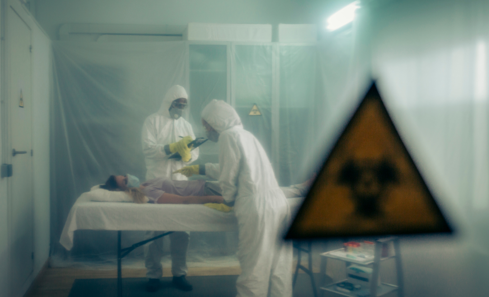Doctors standing over infected person in protective medical suits.